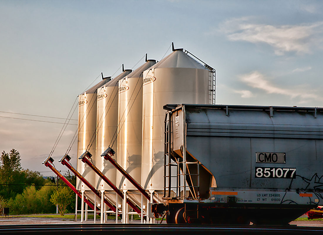 About Our Agency - End of a Train Parked Next to Four Water Storage Towers at Sunset with a Cloudy Blue Sky