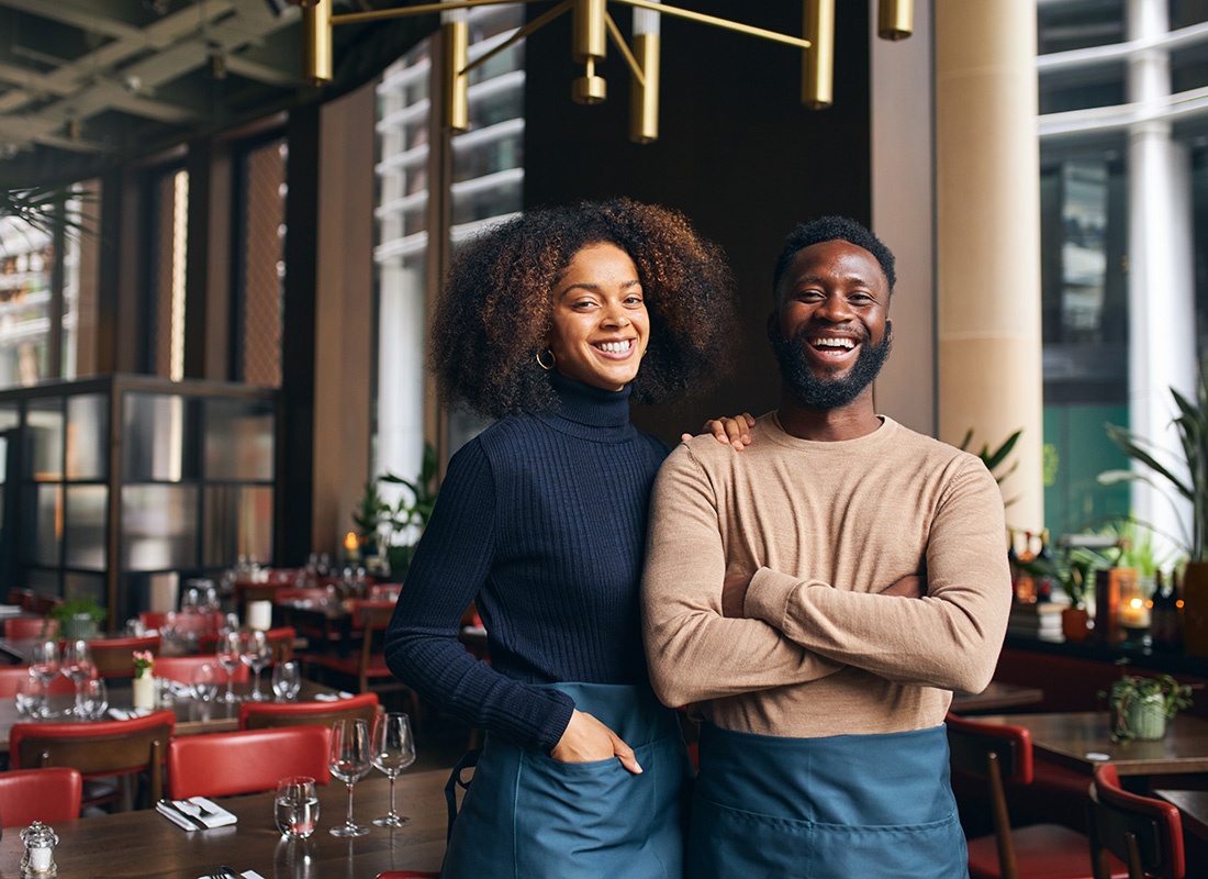Business Insurance - Portrait of Two Cheerful Young Business Owners Standing Next to Empty Tables Inside Their Restaurant