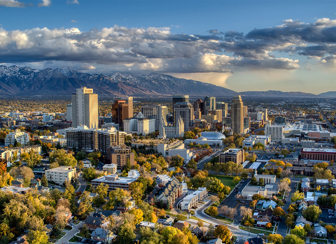 Contact - Aerial View of Downtown Salt Lake City Utah Buildings Surrounded by Green Foliage with Low Hanging Clouds and Mountains in the Background