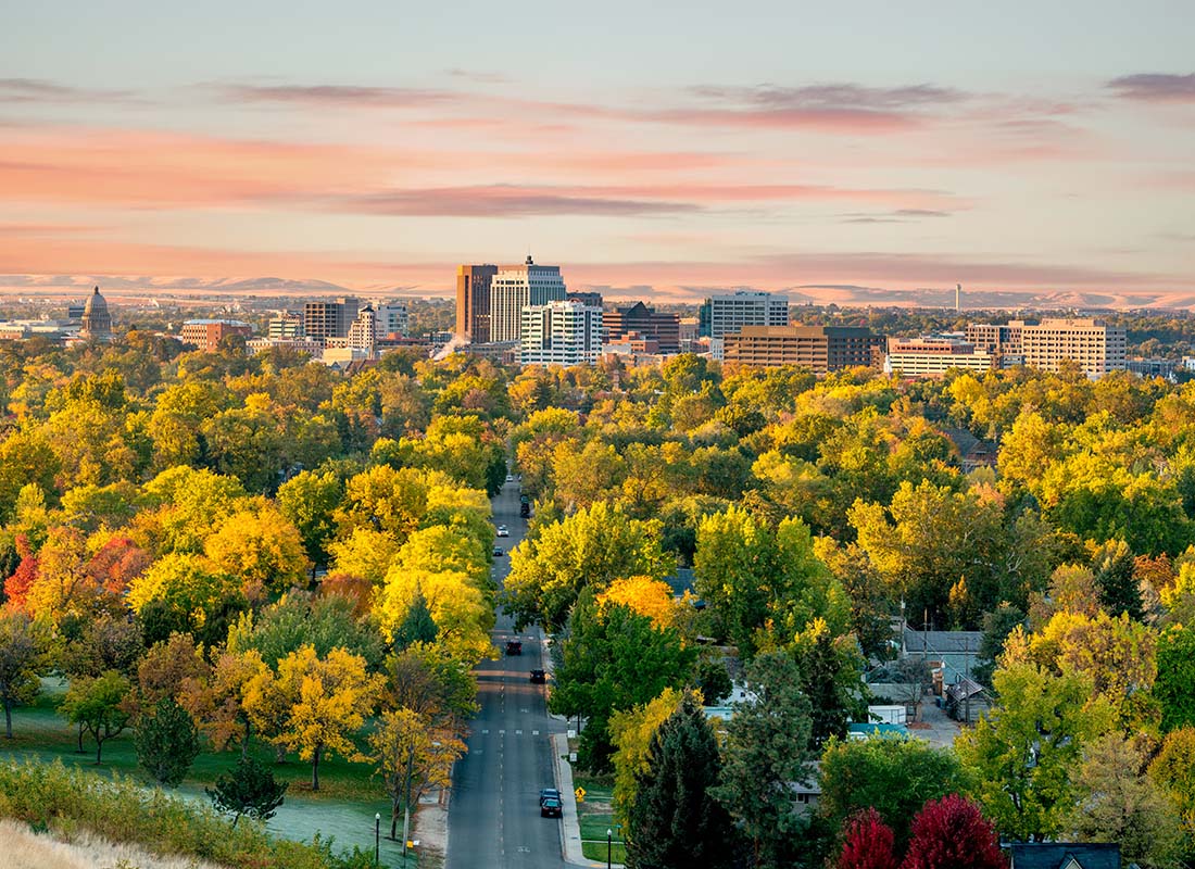 We Are Independent - Scenic View of Colorful Trees During the Fall in Boise Idaho with Commercial Buildings Visible in the Background Against a Colorful Sunset Sky